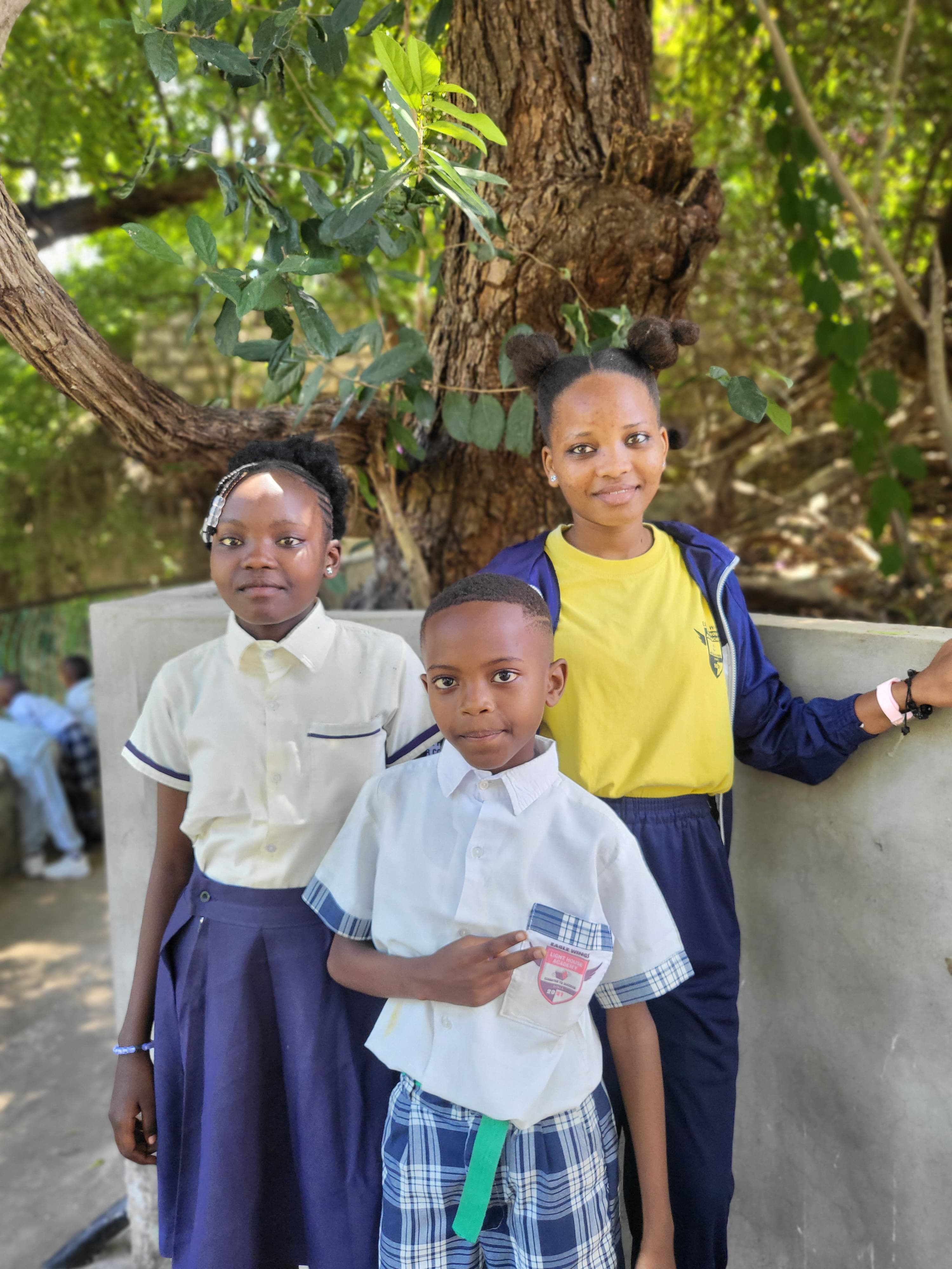 Three students posing under a tree on the Mamba Village grounds